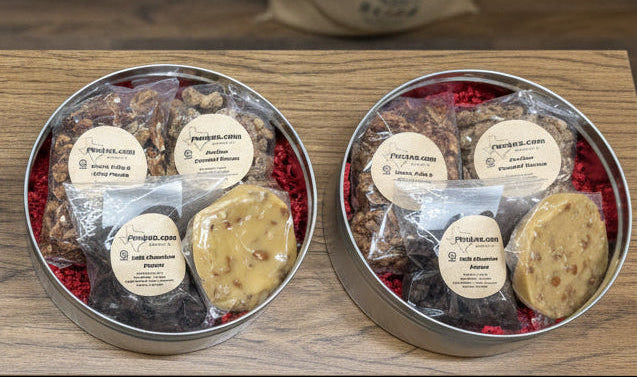 Four tins of assorted cookies on a wooden shelf with bags of coffee in the background.