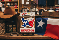 Texas-themed display with a hat, thermometer, and flag on a wooden shelf.